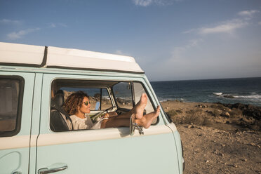 Spanien, Teneriffa, Frau sitzt mit hochgelegten Füßen in einem am Meer geparkten Lieferwagen - SIPF01736