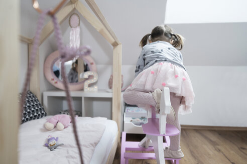 Kleinkind Mädchen klettert auf Schaukelpferd im Kinderzimmer - SBOF00599