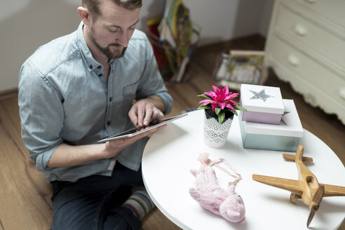 Vater sitzt auf dem Boden im Kinderzimmer und schaut auf ein Tablet - SBOF00601