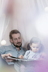 Father and daughter looking at photo album in toy teepee - SBOF00604