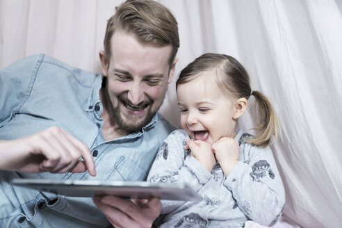 Vater und seine kleine Tochter schauen auf ein Tablet und lachen zusammen - SBOF00608