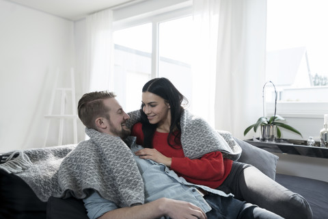 Ehepaar kuschelt unter einer Decke auf dem Sofa im Wohnzimmer, lizenzfreies Stockfoto