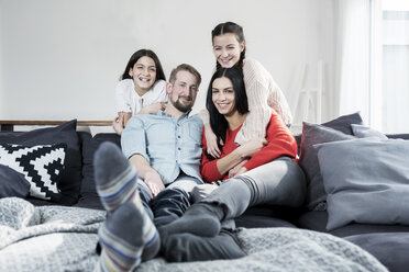 Family portrait of parents and twin daughters on sofa in living room - SBOF00629