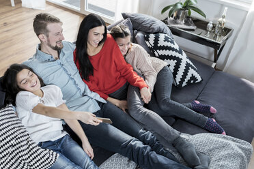 Happy parents and twin daughters on sofa in living room watching Tv - SBOF00631