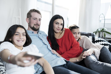 Parents and twin daughters on sofa in living room watching Tv - SBOF00632