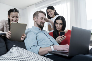 Parents and twin daughters on sofa using portable devices - SBOF00633