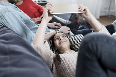 Girl with family lying on sofa holding tablet - SBOF00635