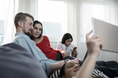 Familie auf dem Sofa sitzend mit Zwillingstöchtern, die Tablet und Smartphone halten - SBOF00636