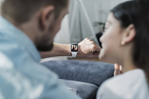 Tochter und Vater schauen auf eine Smartwatch, während die Mutter ihnen zuwinkt - SBOF00639