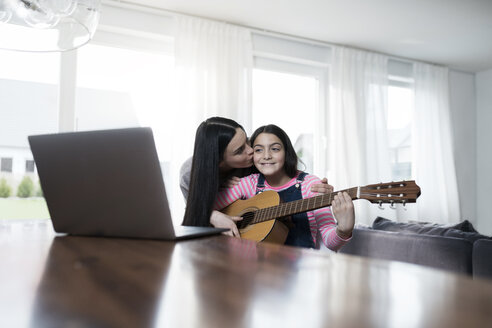 Mutter küsst Tochter, die vor einem Laptop Gitarre spielt - SBOF00643