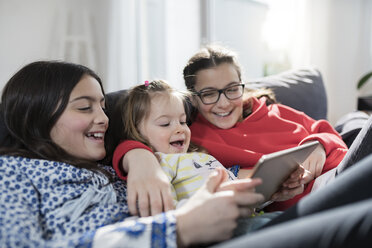 Drei Schwestern lächelnd und mit Tablet auf dem Sofa im Wohnzimmer - SBOF00660