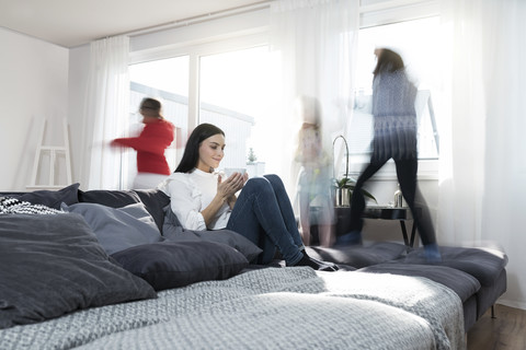 Mädchen springen auf dem Sofa, während die Mutter eine Tasse Tee trinkt, lizenzfreies Stockfoto