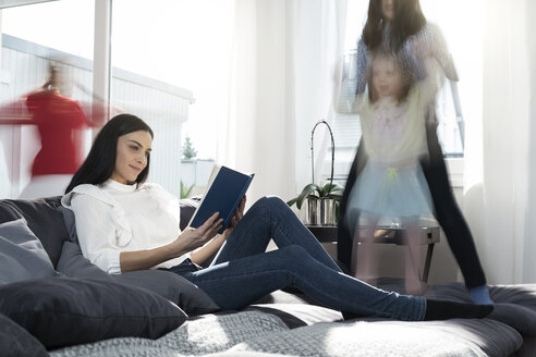 Mädchen springen auf dem Sofa, während die Mutter ein Buch liest - SBOF00662