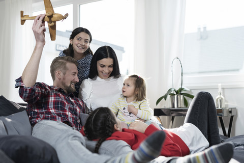Parents and three daughers playing with toy plane on sofa stock photo