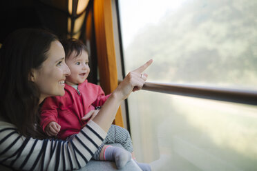 Happy mother and baby girl traveling by train looking out of window - GEMF01804