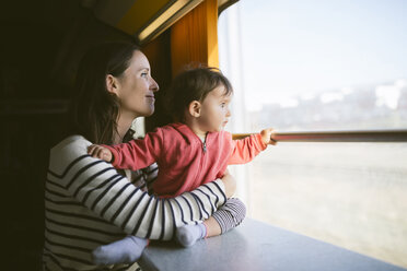 Mother and baby girl traveling by train looking out of window - GEMF01805