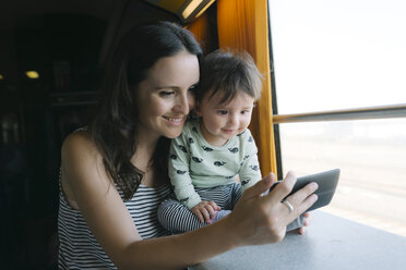 Glückliche Mutter und kleines Mädchen benutzen ihr Smartphone während einer Zugfahrt - GEMF01806
