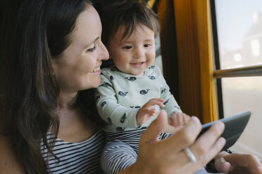 Glückliche Mutter und kleines Mädchen benutzen ihr Smartphone während einer Zugfahrt - GEMF01808