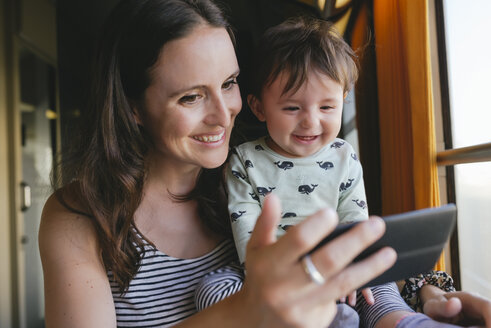 Happy mother and baby girl using smartphone while traveling by train - GEMF01809