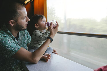 Father giving water to his baby girl in a baby bottle while traveling by train - GEMF01810