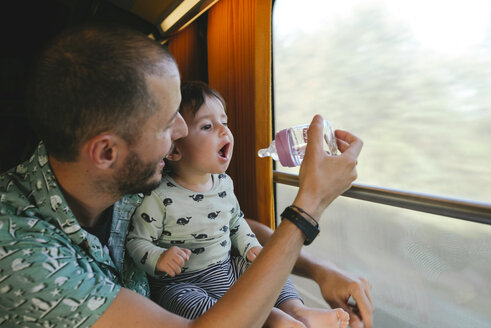 Vater gibt seinem kleinen Mädchen während einer Zugfahrt Wasser in einer Babyflasche - GEMF01811