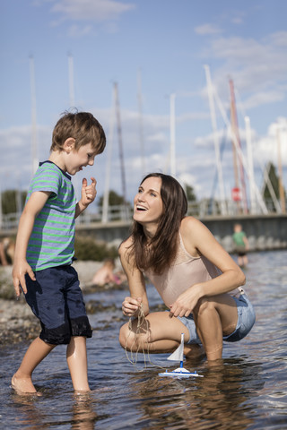 Germany, Friedrichshafen, Lake Constance, happy mother and son with toy boat at lakeshore stock photo