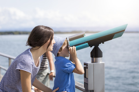 Germany, Friedrichshafen, Lake Constance, mother with son looking through telescope at lakeshore stock photo