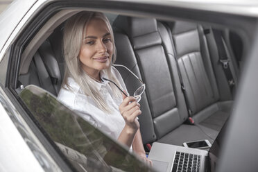 Lächelnde Geschäftsfrau mit Brille benutzt Laptop im Auto - VPIF00042