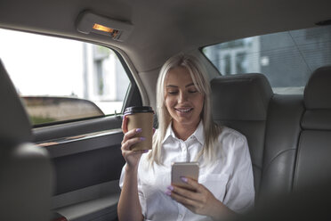 Smiling businesswoman with takeaway coffee and cell phone in car - VPIF00044