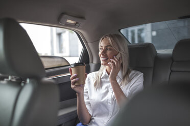 Smiling businesswoman with takeaway coffee on cell phone in car - VPIF00045