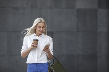 Smiling businesswoman with takeaway coffee and cell phone on the move - VPIF00054