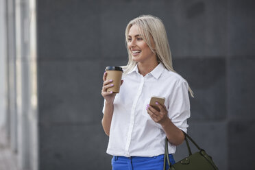 Happy businesswoman with takeaway coffee and cell phone outdoors - VPIF00055