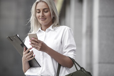 Lächelnde Geschäftsfrau mit Klemmbrett und Mobiltelefon im Freien - VPIF00057