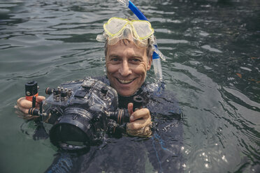 Porträt eines glücklichen Mannes mit Unterwasser-DSLR-Kameragehäuse in einem See - MFF03929