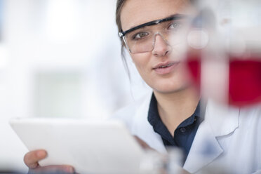 Scientist working in lab holding a tablet looking at flask - ZEF14596