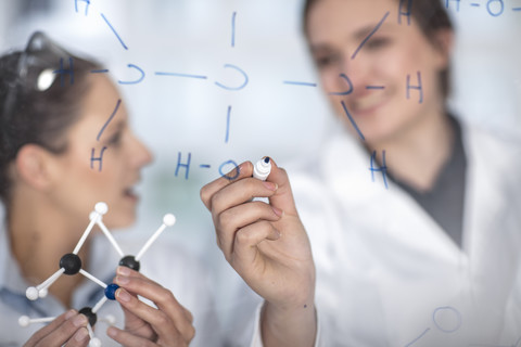 Zwei Wissenschaftler arbeiten im Labor und schreiben Notizen auf eine Glasscheibe, lizenzfreies Stockfoto