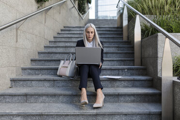 Junge Geschäftsfrau sitzt auf einer Treppe in der Stadt und benutzt einen Laptop - GIOF03214