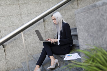 Junge Geschäftsfrau sitzt auf einer Treppe in der Stadt und benutzt einen Laptop - GIOF03215