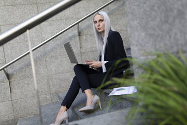 Young businesswoman sitting on stairs in the city using laptop - GIOF03216