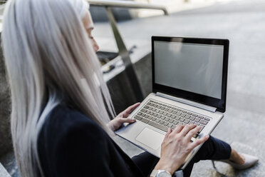 Young businesswoman sitting on stairs in the city using laptop - GIOF03217