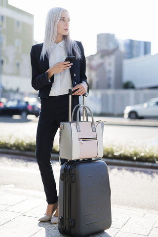 Junge Geschäftsfrau in der Stadt mit Handy und Gepäck, lizenzfreies Stockfoto