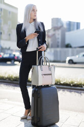 Young businesswoman in the city with cell phone and luggage - GIOF03231