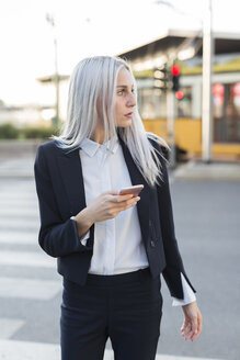 Junge Geschäftsfrau in der Stadt mit Mobiltelefon, die sich umschaut - GIOF03237