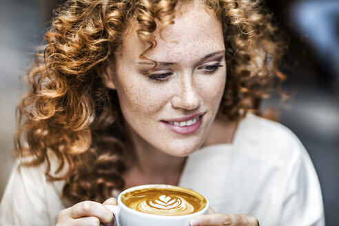 Porträt einer lächelnden jungen Frau mit Cappuccino - FMKF04479