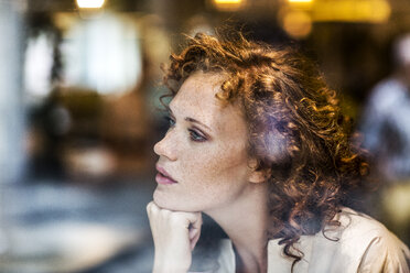 Porträt einer nachdenklichen jungen Frau hinter einer Fensterscheibe - FMKF04483