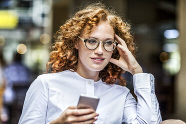 Porträt einer lächelnden jungen Frau mit Mobiltelefon - FMKF04484