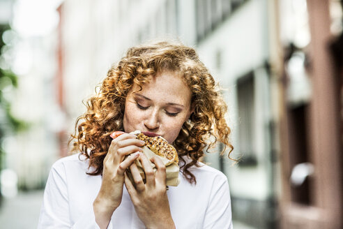 Porträt einer jungen Frau, die einen Bagel im Freien isst - FMKF04487