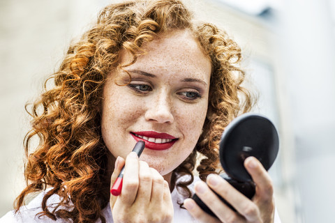 Portrait of freckled young woman applying lipstick stock photo