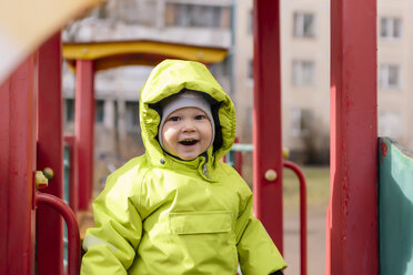 Porträt eines glücklichen Kleinkindes mit Regenjacke auf dem Spielplatz - KNTF00882