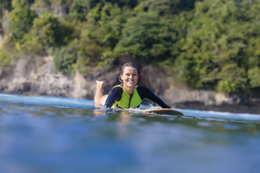 Indonesien, Bali, lächelnde Frau auf Surfbrett liegend - KNTF00889